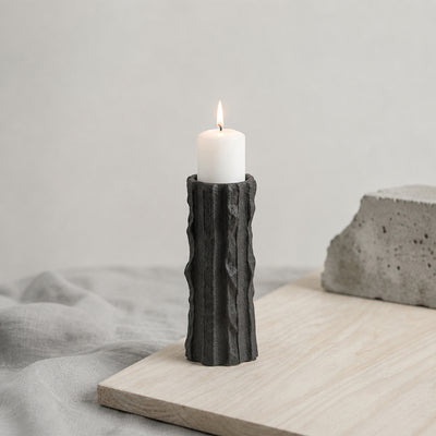 Black textured candle holder with white candle placed on table for modern contemporary decor styling.