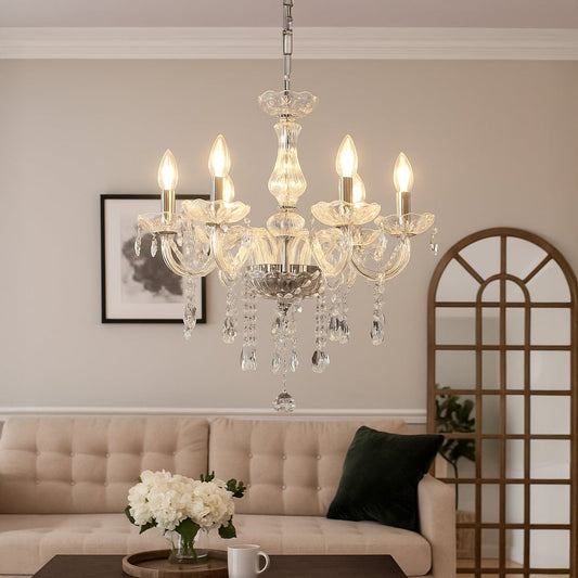 Crystal chandelier glowing warmly in a modern living room with beige sofa wall art mirror and floral table decor.