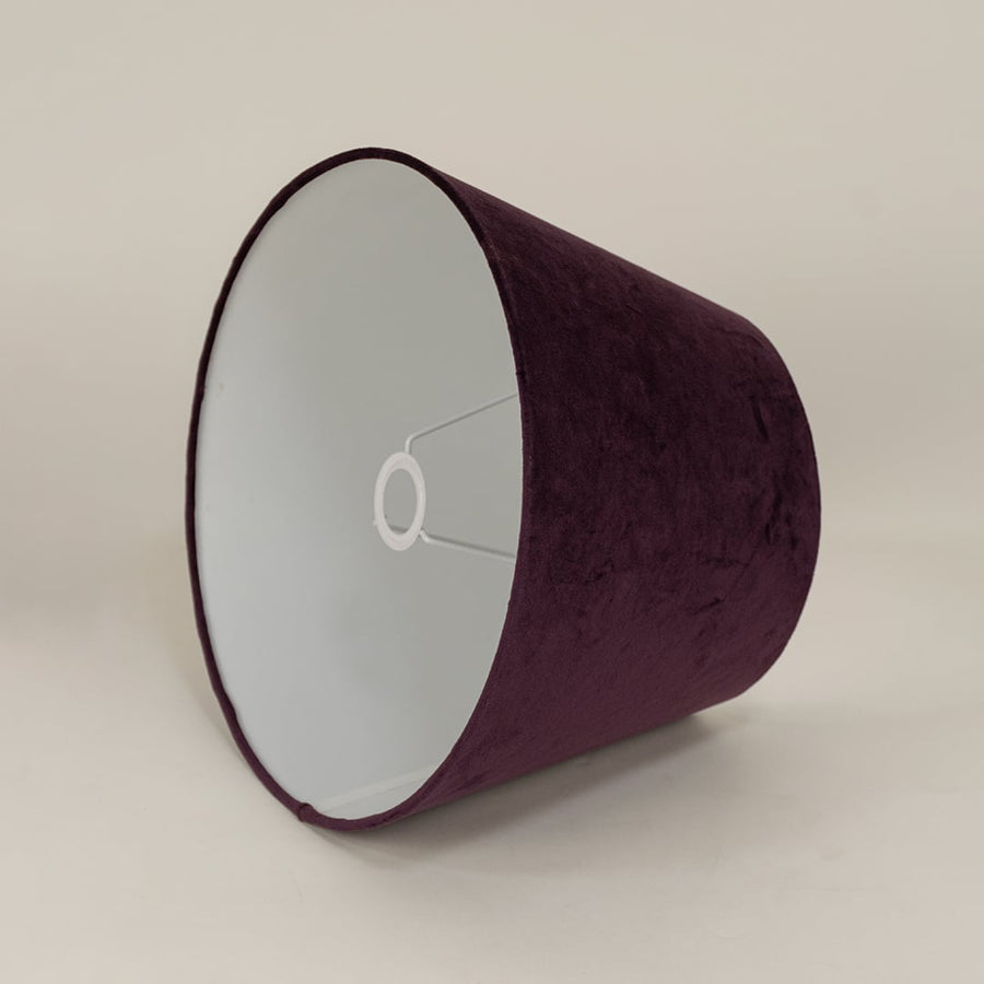 Modern plum velvet lampshade standing against a plain white background capturing its soft surface and simple elegant form.