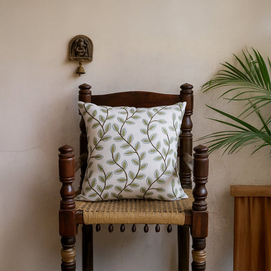 Soft cotton cushion cover with green botanical embroidery styled on a wooden chair offering a natural décor accent with a breathable gentle and skin friendly fabric finish ideal for modern homes.