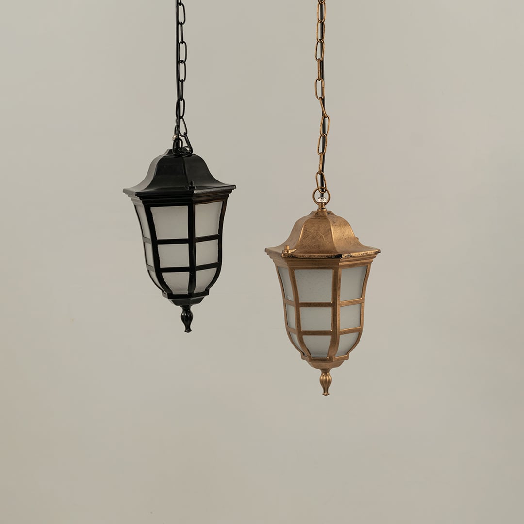 Pair of classic hanging lantern lamps one black and one antique brass finish suspended together with lights off against a plain background.