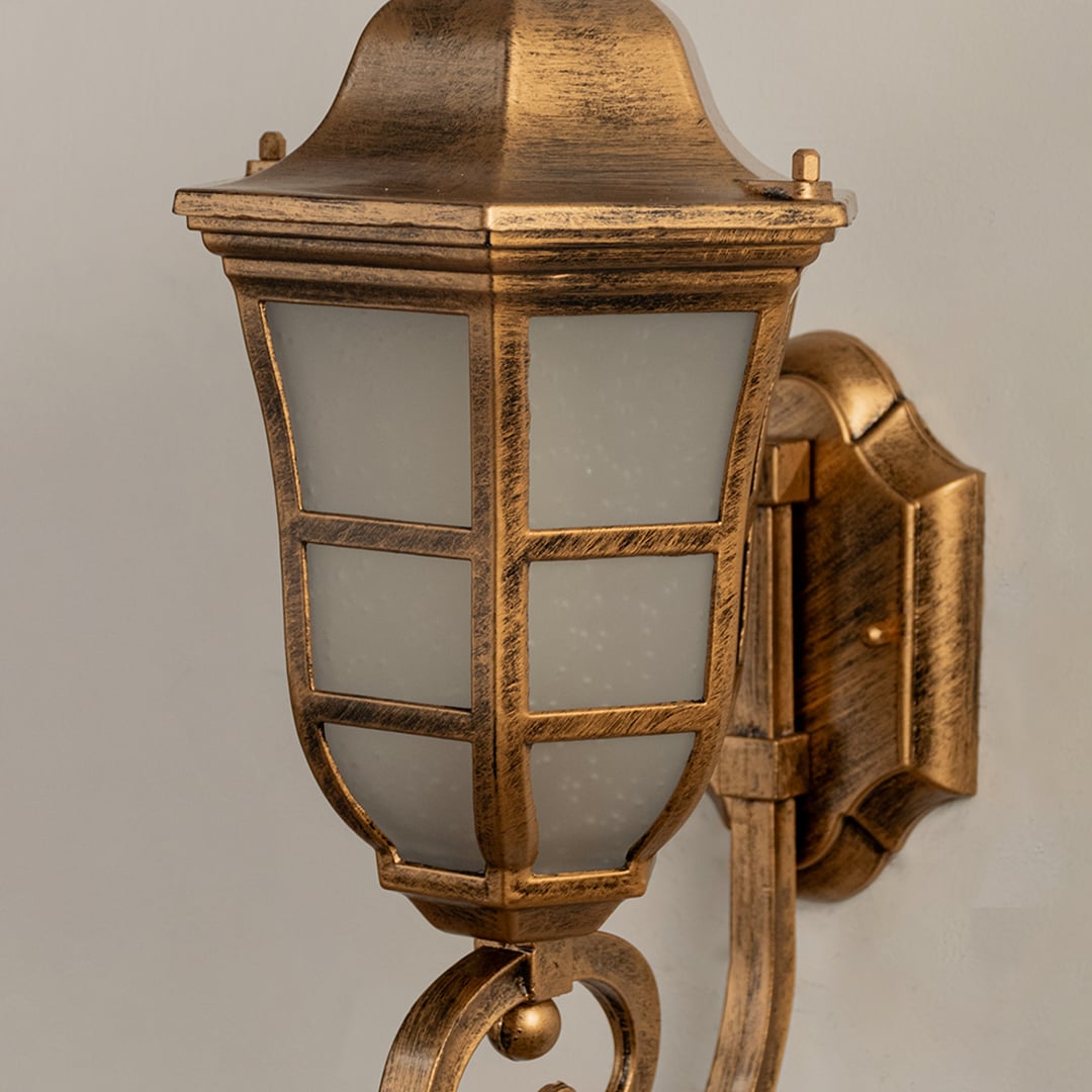 Closeup of gold metal outdoor lantern showing warm frosted glow and ornate curved arm perfect for enhancing porch patio and home entrance Decor.