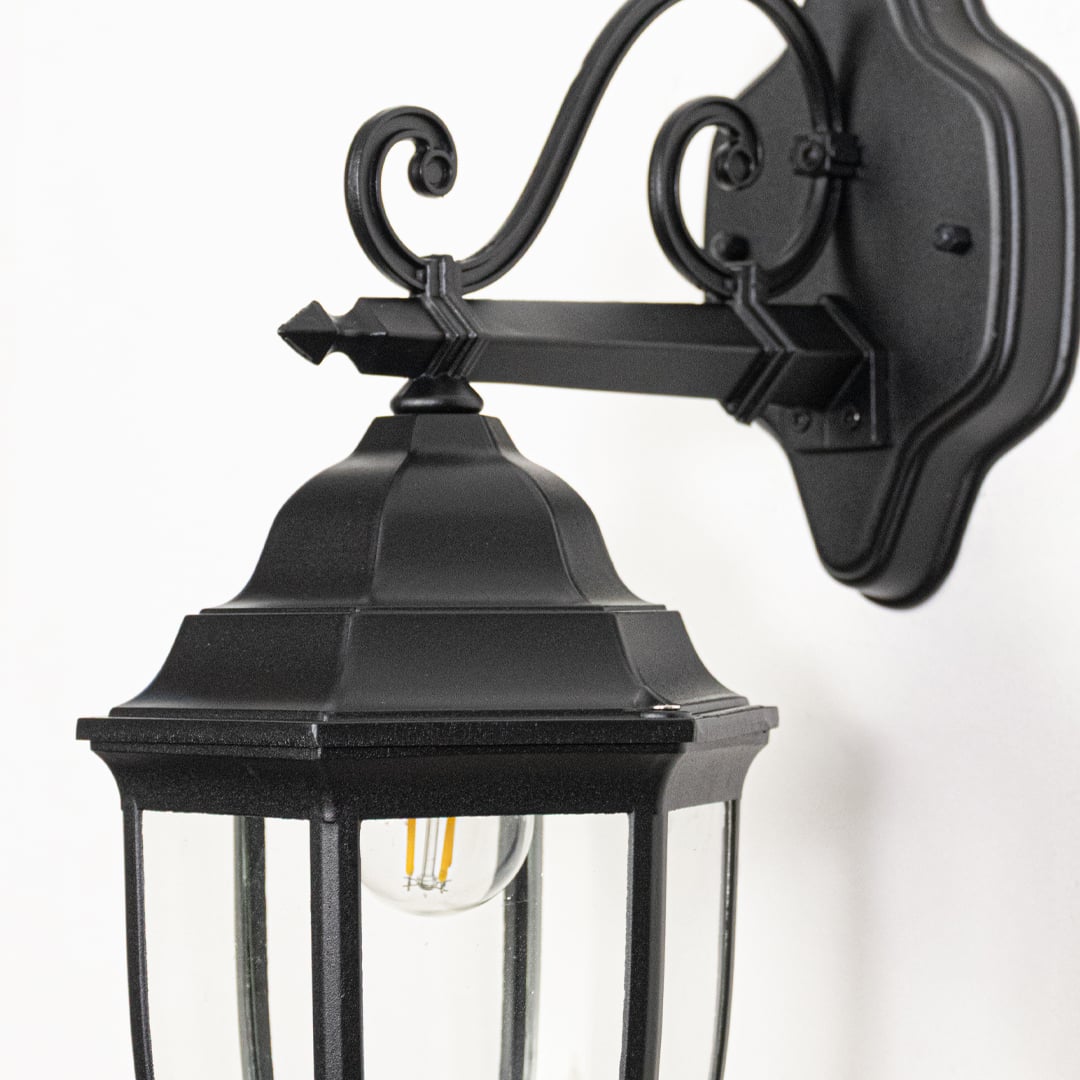 Closeup image of Victorian outdoor wall light facing downward in black metal highlighting ornate design glass shade and exterior wall use.