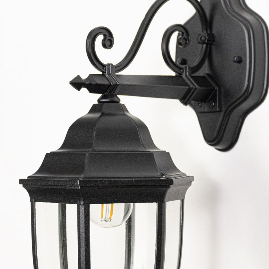Closeup image of Victorian outdoor wall light facing downward in black metal highlighting ornate design glass shade and exterior wall use.