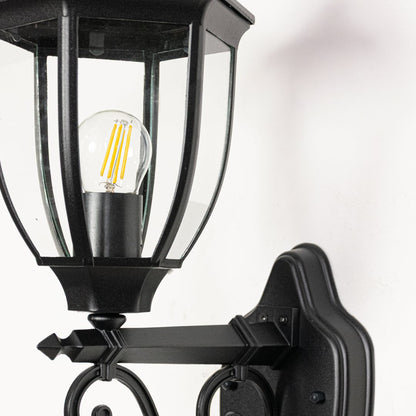 Closeup of Victorian style outdoor wall light facing upward in black metal showing decorative curves glass detail and classic exterior charm.