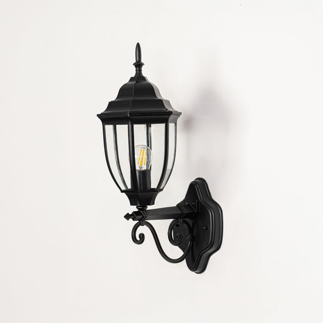 Outdoor wall light switched off on white background highlighting lantern shape glass panels metal finish and decorative mounting arm.
