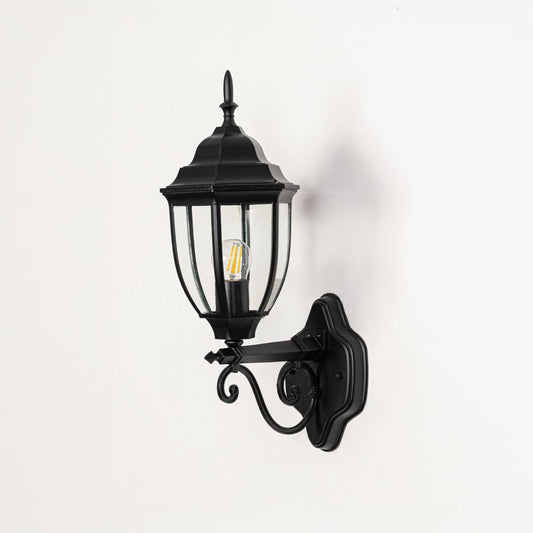 Outdoor wall light switched off on white background highlighting lantern shape glass panels metal finish and decorative mounting arm.