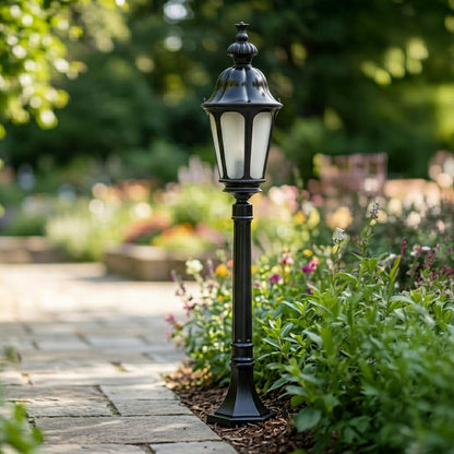 Classic black outdoor garden pole light with lantern design installed along pathway with greenery ideal for landscape and pathway lighting.