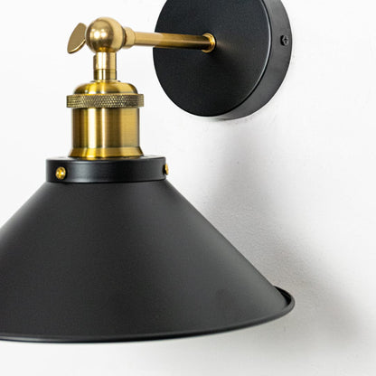 Black metal wall light closeup highlighting matte cone shade and brass arm detailing for modern industrial interior lighting.