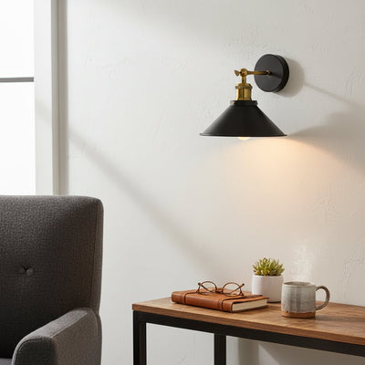 Black metal wall light with gold metal accents mounted above side table creating warm ambient lighting for modern bedroom reading corner decor.