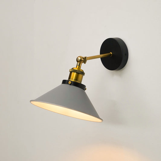 A modern wall-mounted sconce with a gray conical shade, gold-toned metal arm and collar, and a round black wall plate, shown lit against a plain light wall.