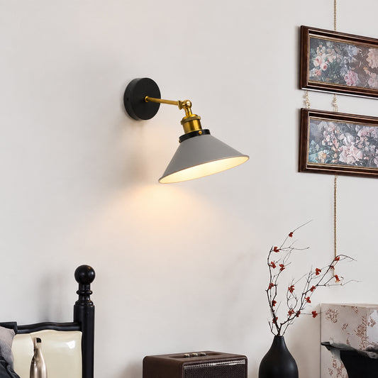A wall-mounted swing-arm sconce lamp with a matte black round backplate, gold-toned metal arm, and a gray conical shade, shown lit on a white wall in a styled interior setting.