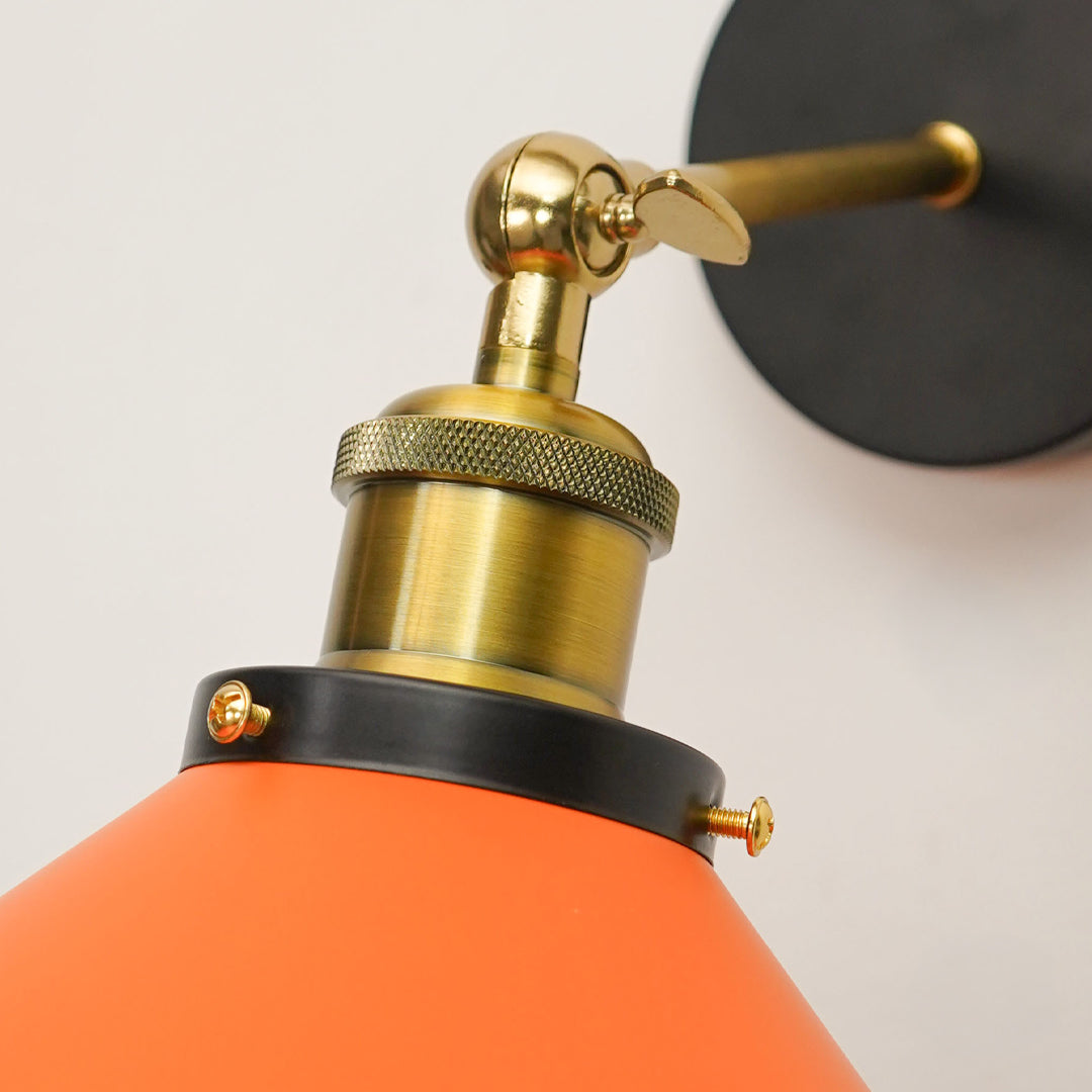 Close-up of a modern wall lamp featuring a bright orange cone-shaped shade, a brushed brass pump-style neck with a brass lever, and a black wall mount disc on a white background.
