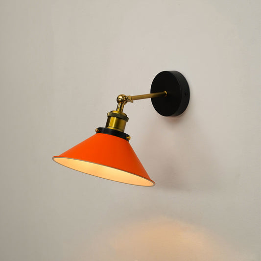 A modern wall-mounted sconce with a bright orange cone-shaped shade, a black circular wall plate, and a brass-toned adjustable arm, shown lit against a plain light gray wall.