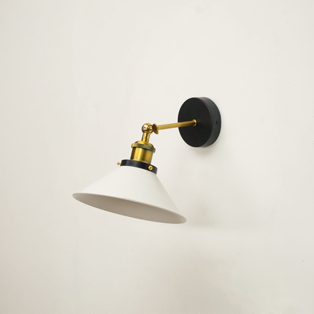 A modern wall-mounted sconce light fixture with a white conical shade, a polished brass arm and collar, and a round black wall plate, shown against a plain off-white wall.