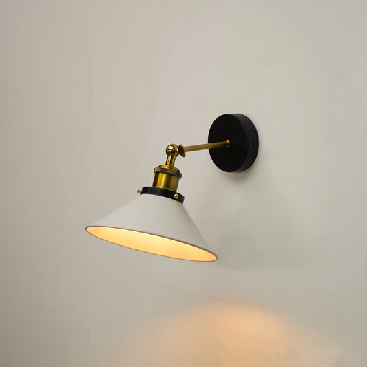A modern wall-mounted sconce with a white conical shade, a black circular wall plate, and a brass-finished adjustable arm, shown lit against a plain light gray wall.