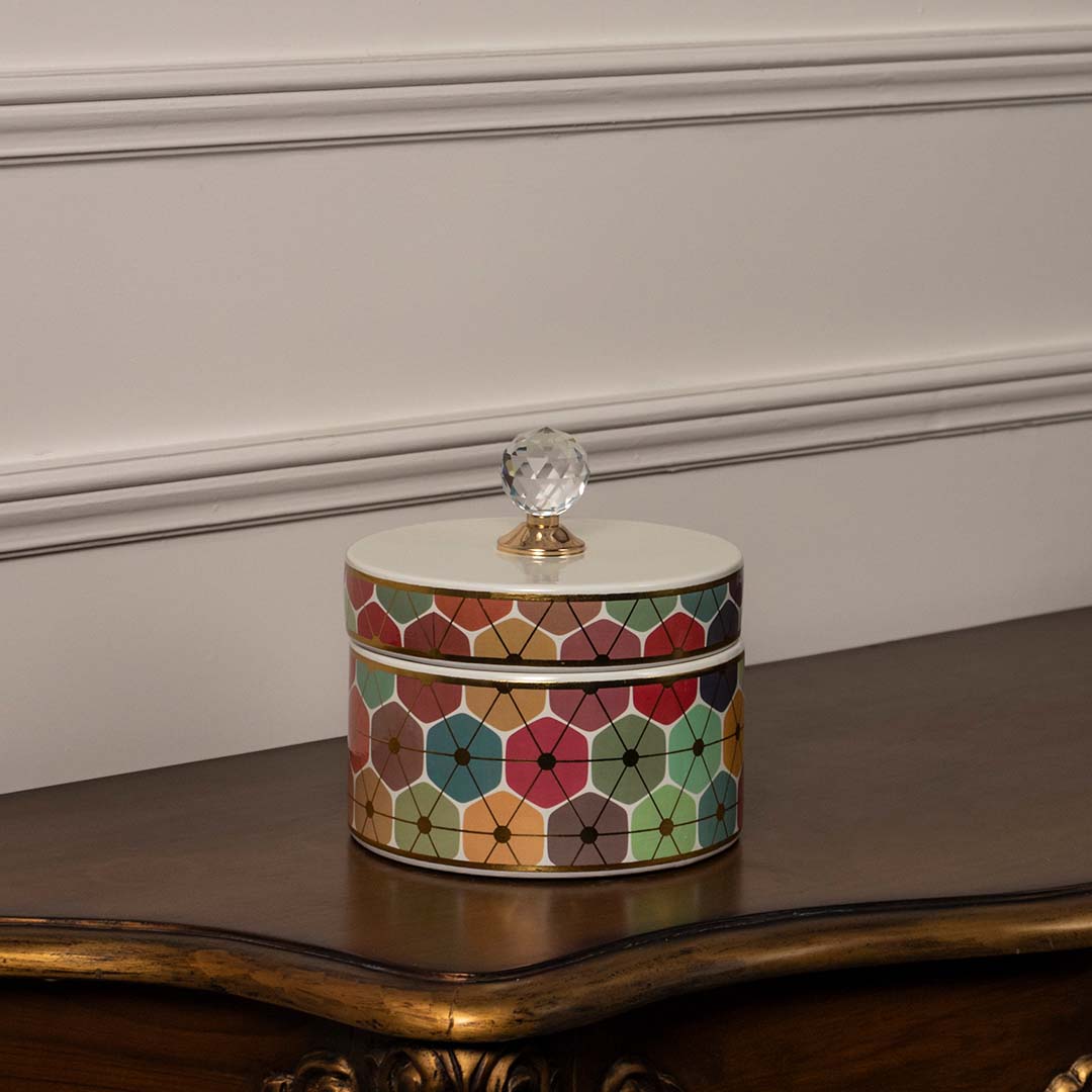 Decorative ceramic jar with multicolor floral artwork and glass lid placed on wooden table against neutral wall background highlighting premium decorative storage styling.
