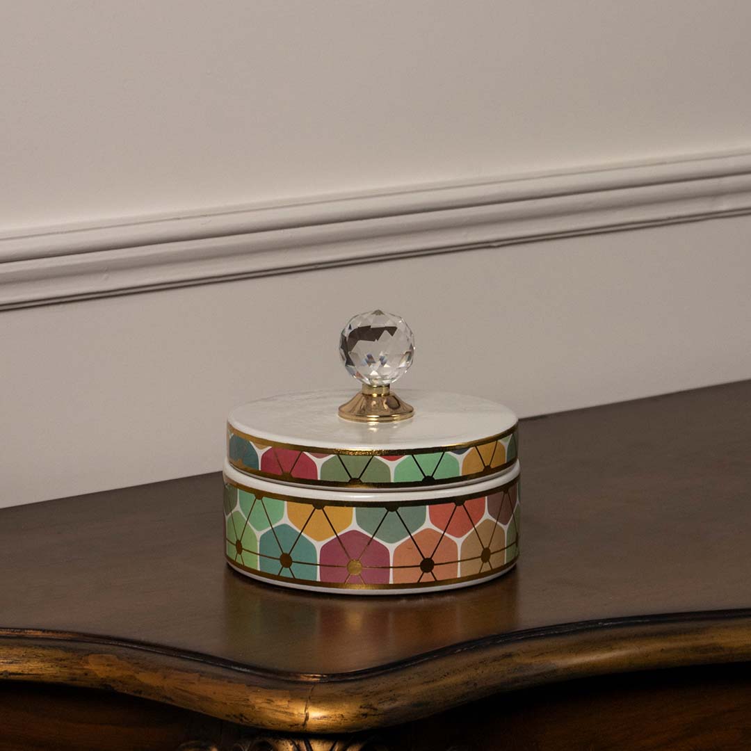 Round ceramic jar with colorful floral pattern and glass knob lid placed on wooden table against neutral wall background showcasing vibrant artistic home decor appeal.