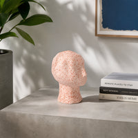 Pink textured ceramic face sculpture placed on table beside books for stylish contemporary home decor.