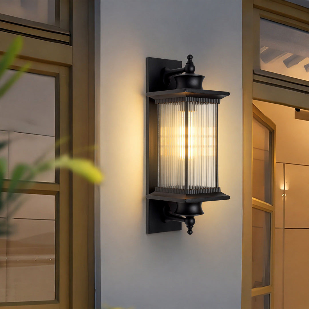 Modern black metal outdoor wall light lifestyle image with reeded glass shade mounted by a courtyard glass entry door.