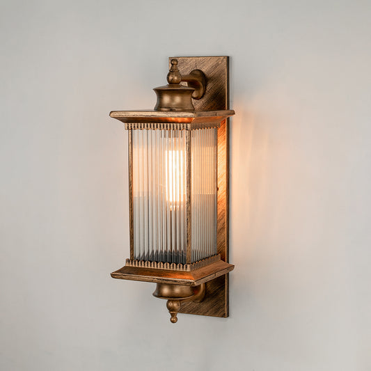 Antique brass metal outdoor wall light on white background with ribbed glass shade illuminating warm patio decor.
