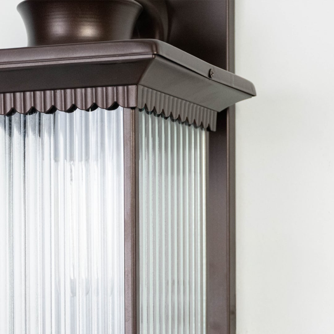 Closeup image of black metal outdoor wall light with ribbed glass shade for modern exterior decor.