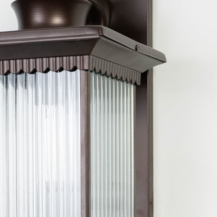 Closeup image of black metal outdoor wall light with ribbed glass shade for modern exterior decor.