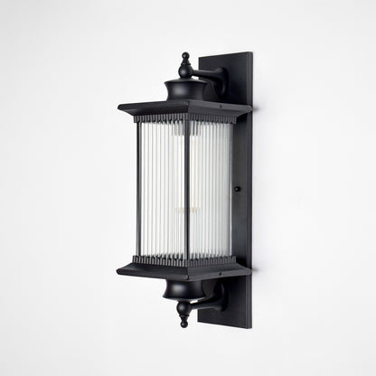 Black aluminum outdoor wall light on white background with a vertical reeded glass shade for modern patio decor.
