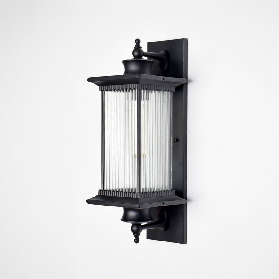 Black aluminum outdoor wall light on white background with a vertical reeded glass shade for modern patio decor.