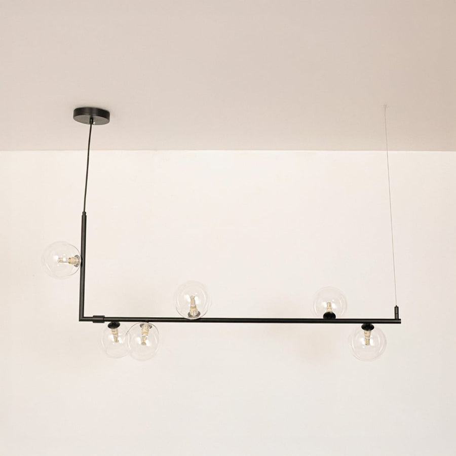 Black linear chandelier with clear glass globes displayed on a white background with lights off showing clean form.