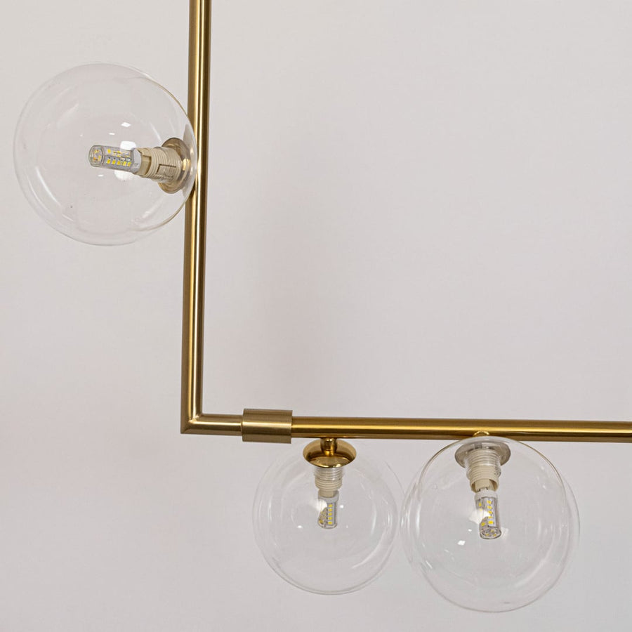 Closeup of gold linear chandelier with clear glass globes highlighting sleek metal finish and refined globe details.