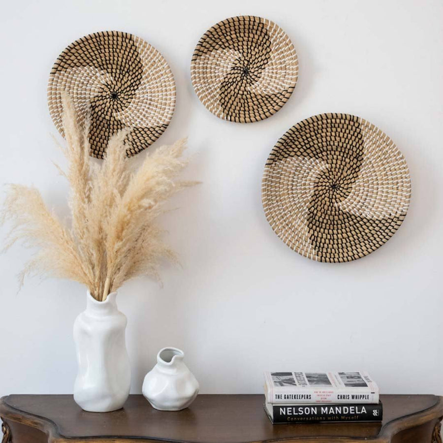 Grouped woven wall baskets styled above wooden console table with white vase for rustic living room wall accent display.