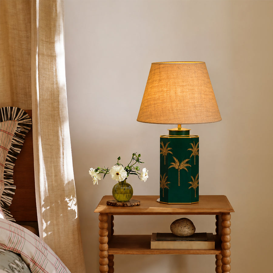 Green floral table lamp with beige fabric shade casting warm ambient light on wooden side table in elegant interiors.