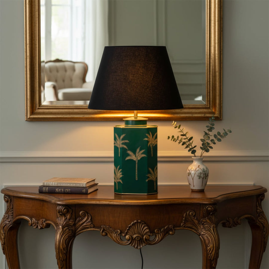 Green ceramic bedside table lamp with black fabric shade placed on wooden console for warm ambient home lighting.