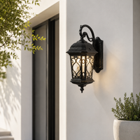 Ornate black iron decorative scroll grid glass carriage wall lantern on white stucco facade for residential patio entryway.