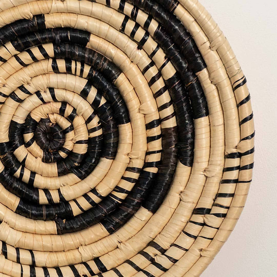 Detailed closeup of handcrafted black cream woven seagrass wall basket with swirling vortex spiral pattern for boho decor.