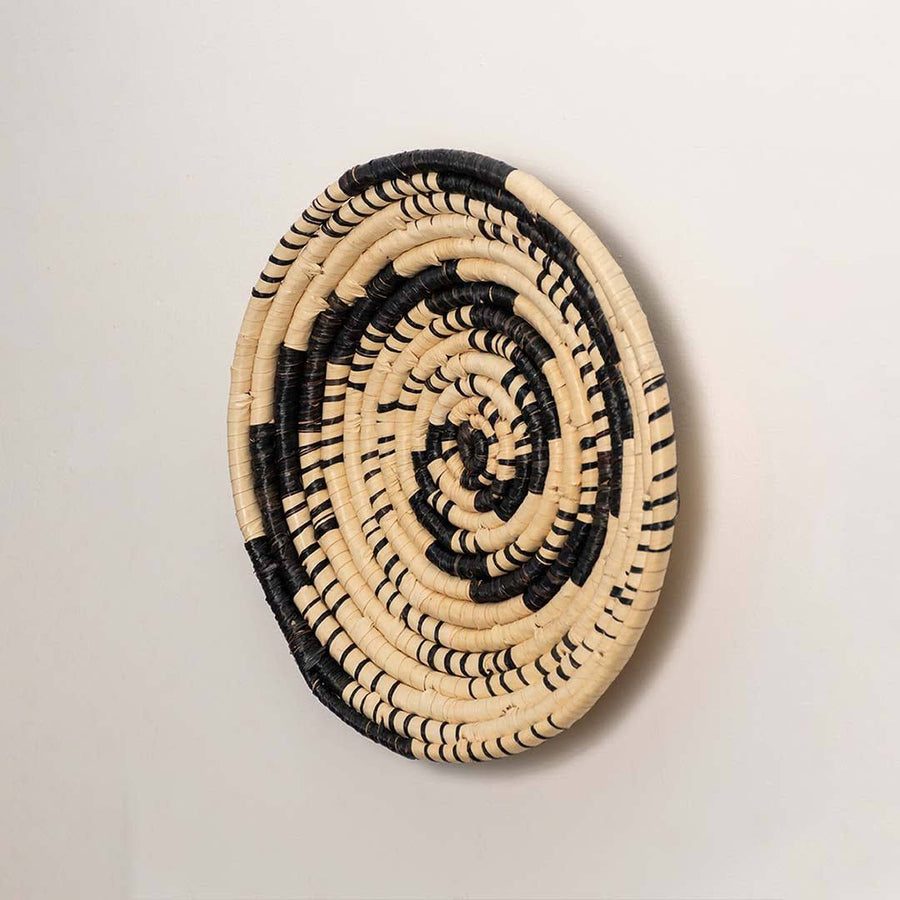 Side view of handcrafted black cream woven seagrass wall basket with swirling vortex spiral pattern for bohemian wall decor.