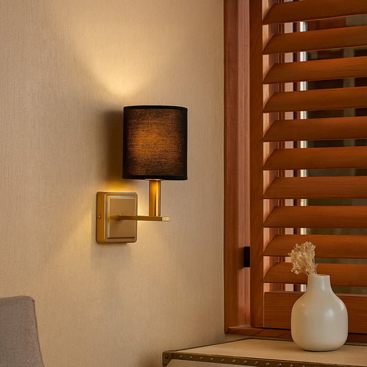 Gold wall sconce with black drum shade styled in a modern interior for elegant warm ambient lighting decor.