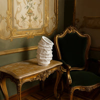 Eclipse white ceramic vase with sculptural textured finish styled on a vintage gold table beside a green velvet chair adding elegance to classic interiors.