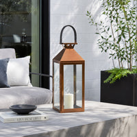 Modern copper metal lantern with clear glass panels and top handle creating elegant candlelight for outdoor table settings.