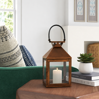 Modern copper metal candle lantern with clear glass panels adding warm decorative lighting to cozy indoor living spaces.