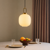 Modern brass arch and white frosted glass globe pendant light hanging above a minimalist dining table setting.