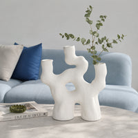 White abstract ceramic flower vase with green stems placed on marble table for stylish home decor.