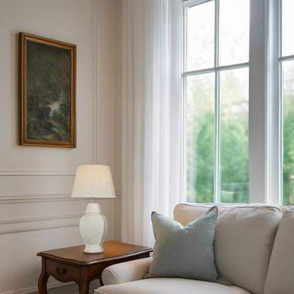 White ceramic textured table lamp with a soft cream shade placed on a wooden side table adding a bright elegant touch to modern living room decor.