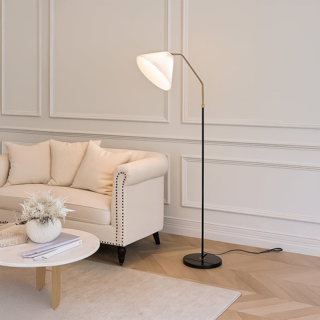 Living room setup featuring a white pleated shade floor lamp beside a beige sofa with a neutral rug and decorative plants.