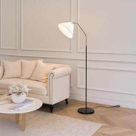 Living room setup featuring a white pleated shade floor lamp beside a beige sofa with a neutral rug and decorative plants.