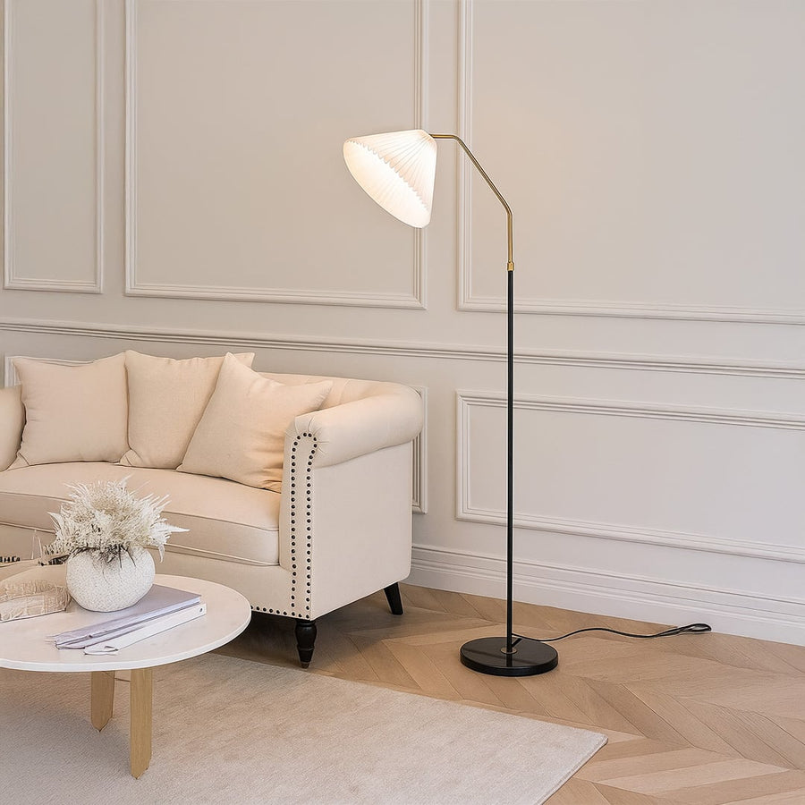 Living room setup featuring a white pleated shade floor lamp beside a beige sofa with a neutral rug and decorative plants.