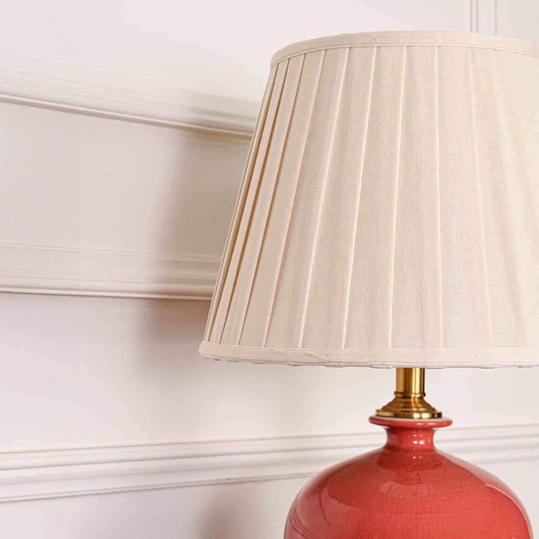 White pleated fabric shade with gold stem detail on red ceramic table lamp highlighting refined decorative elegance.