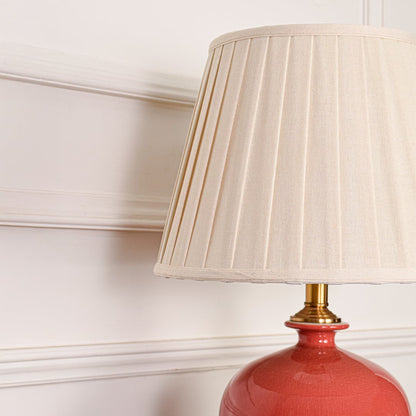 White pleated fabric shade with gold stem detail on red ceramic table lamp highlighting refined decorative elegance.