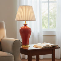 Red ceramic table lamp with cream fabric shade creating warm ambient lighting beside a sofa in elegant living room.